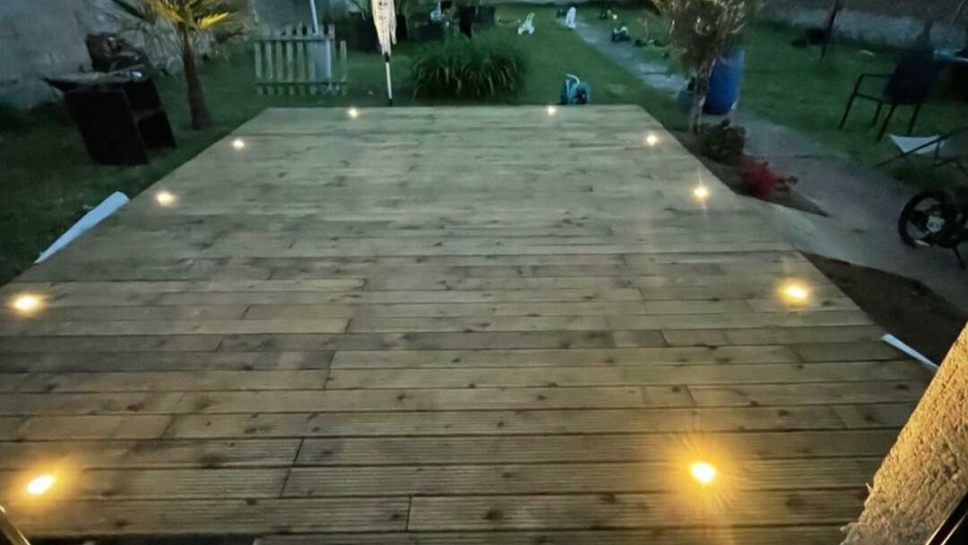 Terrasse en bois éclairée par des spots encastrés au sol, à la tombée de la nuit